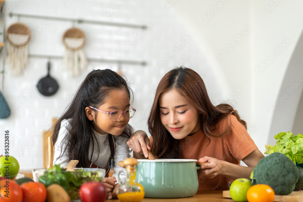 Portrait of happy love asian family mother with little asian girl daughter child help cooking food healthy eat with fresh vegetable testing smell soup in a pot with spoon.help mommy in kitchen at home