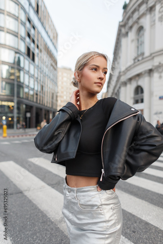 Trendy stylish beautiful young woman in fashion rock clothes with a leather jacket stands on the street
