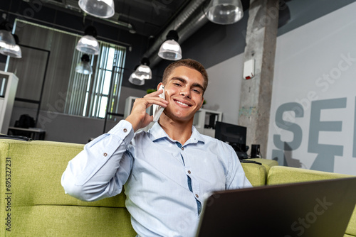 Wallpaper Mural Young businessman talking on the phone while sitting on sofa with laptop in the office Torontodigital.ca