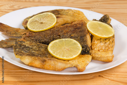 Fried carp pieces on dish, side view on rustic table