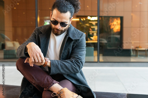Stylish man sitting and checking his watch in the city photo