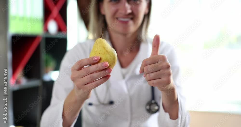 Smiling happy female doctor holding yellow pear and showing thumb up. Nutritionist rockmed fruits medical concept and healthy eating