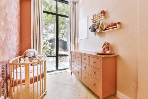 Pink nursery with crib and dresser by bright window
