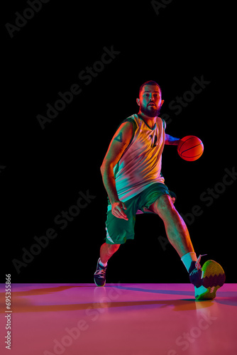 Intense concentration of basketball player during training session, emphasizing commitment to excellence against black background in neon light.