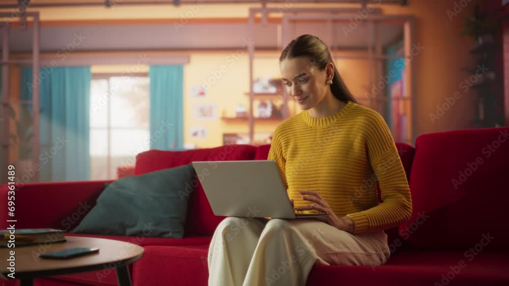 Beautiful Woman Sitting on a Couch in a Cozy Living Room and Using Laptop Computer at Home. Female Smiling and Chatting on Social Media, Doing Online Shopping, Checking the News. Slow Motion Beautiful Woman Sitting on a Couch in a Cozy Living Room and Using Laptop Computer at Home. Female Smiling and Chatting on Social Media, Doing Online Shopping, Checking the News. Slow Motion