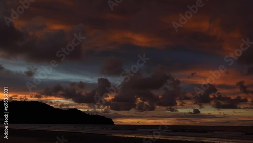 Twilight after sunset. The ocean waves roll towards the shore, foaming. The blue sky is highlighted orange near the horizon. Purple clouds are illuminated by the scarlet light of the sun that has set