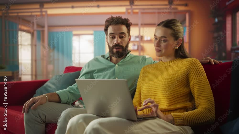 Portrait of Young Couple Using Laptop Computer While Sitting on Couch at Home. Boyfriend and Girlfriend Doing Online Shopping to Renovate the House, Browsing the Internet to Compare Sales Portrait of Young Couple Using Laptop Computer While Sitting on Couch at Home. Boyfriend and Girlfriend Doing Online Shopping to Renovate the House, Browsing the Internet to Compare Sales