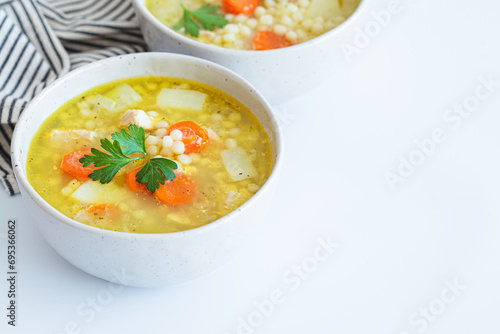 Chicken soup with vegetables and ptimtim - Israeli couscous, white background.