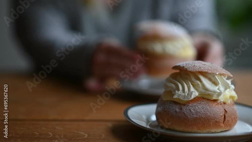 Coffee break with fresh traditional Swedish pastry, known as semla. In the background, out of focus, person eating semlor. Footage made in Sweden.