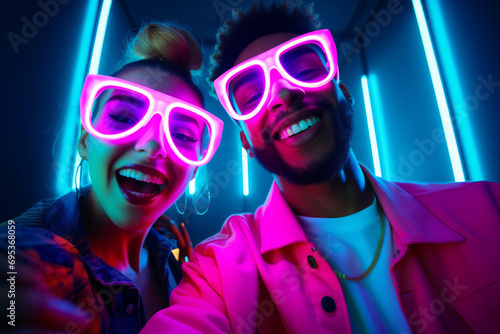group of people in a nightclub. Medium close-up shot of young biracial man with curly hair, in beanie and fun glasses, and Caucasian girl dancing together at house party, with blue and pink neon light