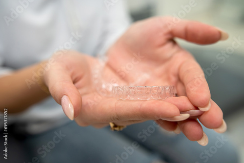 female patient holds two transparent dental aligners in her palms.