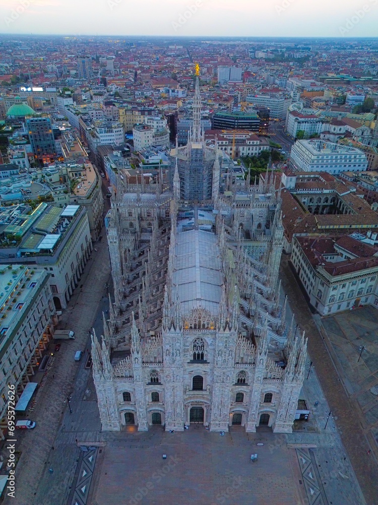 Aerial view of the statue of the Madonna on the central spire of the Duomo and the city's cathedral at dawn. Roofs of houses and skyscrapers. Sun over the horizon. duomo square. Italy Milan 16.11.2023