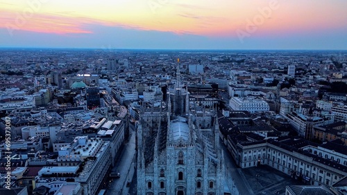Aerial view of the statue of the Madonna on the central spire of the Duomo and the city s cathedral at dawn. Roofs of houses and skyscrapers. Sun over the horizon. duomo square. Italy Milan 16.11.2023