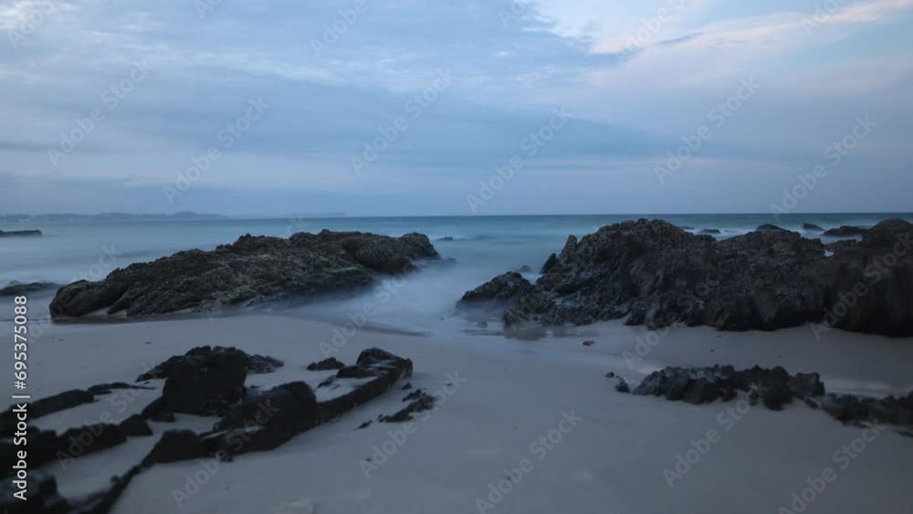 Long exposure of a serene beach with smooth water around rocky outcrops under a twilight sky in Australia Long exposure of a serene beach with smooth water around rocky outcrops under a twilight sky in Australia