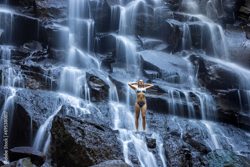 A young woman in a swimming suit at Nungnung waterfall in lush tropical forest  Bali  Indonesia