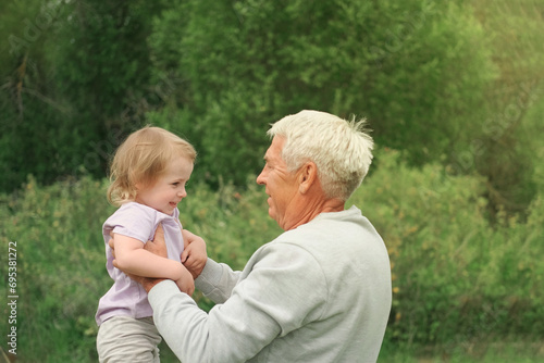 Grandfather and grandchild baby have fun during walk In Park. Happy family. Old man grandpa hugging 2 years child girl at summer day. Smiling Senior male spending time with his granddaughter together
