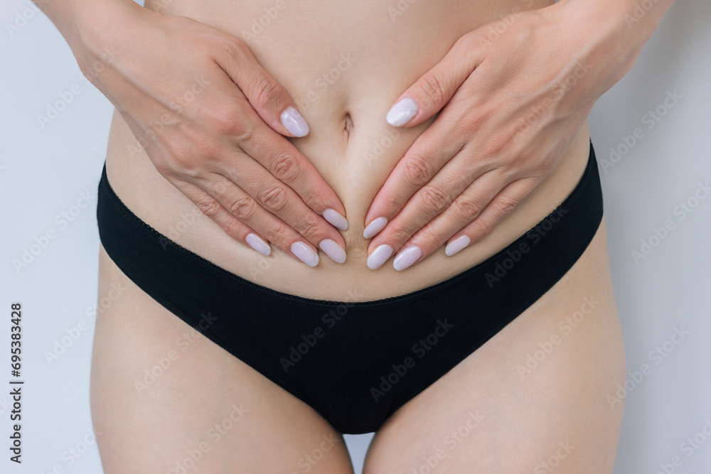 A young woman in black underwear holds her hands to her lower abdomen, suffers from female diseases, cystitis, experiences pain during menstruation. 