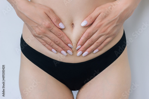 A young woman in black underwear holds her hands to her lower abdomen, suffers from female diseases, cystitis, experiences pain during menstruation.  photo