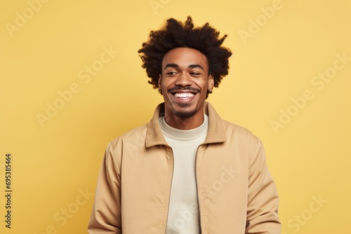 Portrait of a smiling afro-american man in his 20s wearing a trendy bomber jacket against a pastel yellow background. AI Generation © Markus Schröder