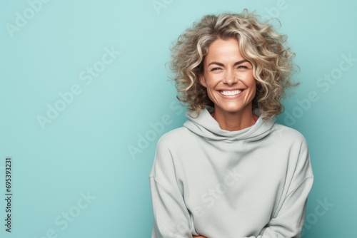 Portrait of a glad woman in her 40s dressed in a comfy fleece pullover against a pastel teal background. AI Generation