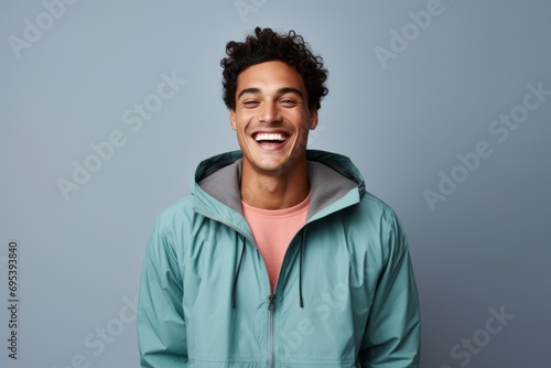 Portrait of a grinning man in his 20s wearing a lightweight packable anorak against a pastel gray background. AI Generation photo