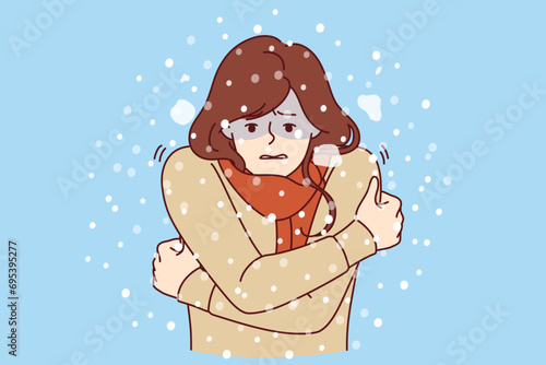 Woman freezes standing under snow in cold winter weather, dressed in sweater and needs warm down jacket or raincoat. Girl is freezing due to lack of outerwear and risks catching cold and flu