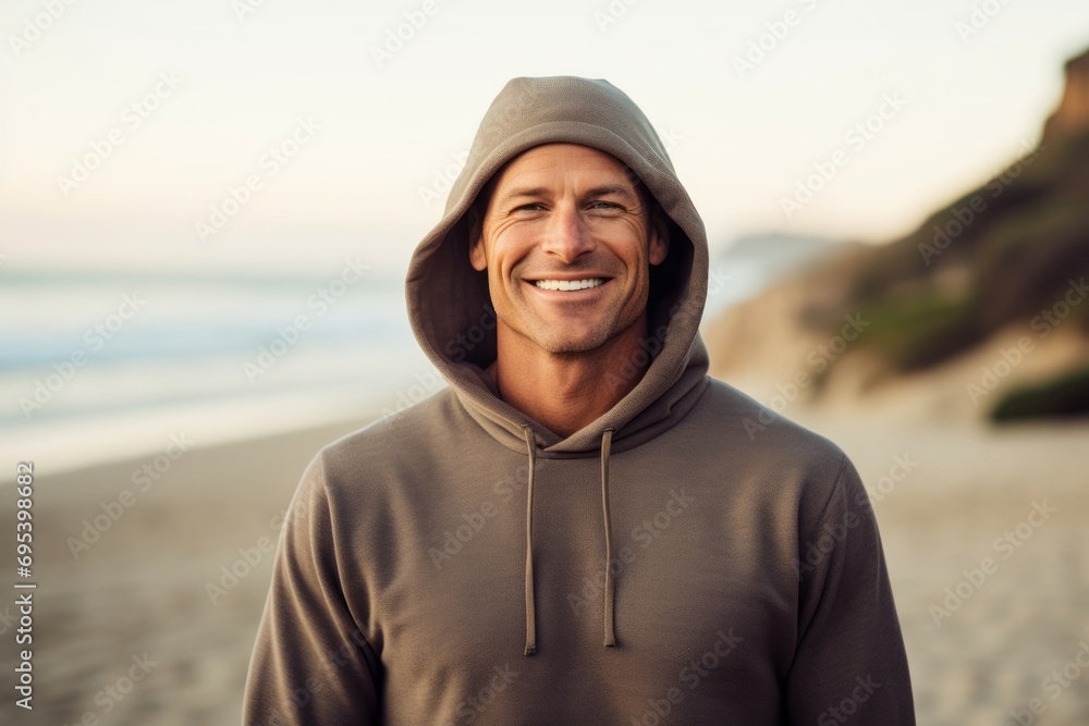 Portrait of a grinning man in his 40s dressed in a comfy fleece pullover against a sandy beach background. AI Generation