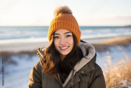 Portrait of a glad asian woman in her 20s dressed in a warm ski hat against a sandy beach background. AI Generation