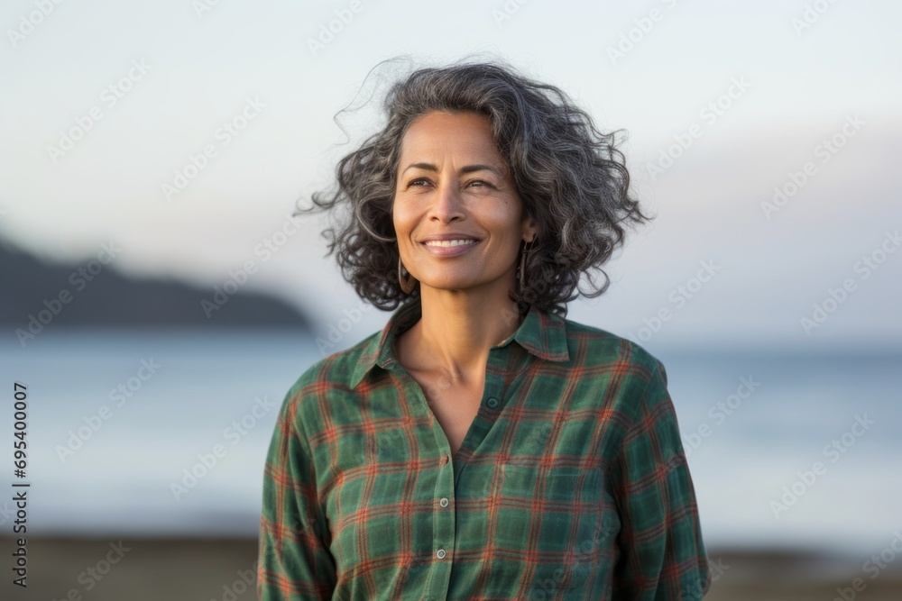 Portrait of a satisfied indian woman in her 50s wearing a comfy flannel shirt against a serene seaside background. AI Generation Portrait of a satisfied indian woman in her 50s wearing a comfy flannel shirt against a serene seaside background. AI Generation