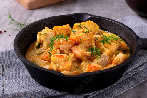 Fish curry with codfish, pollack and shrimps with coconut milk served in cast iron pan photo