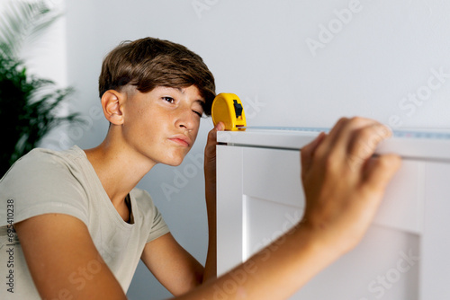 Young teen measuring shelf with yellow measuring tape photo