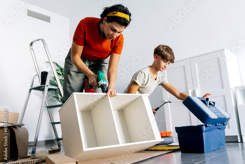 Serious mother with son fixing drawer with electric drill machine during moving photo