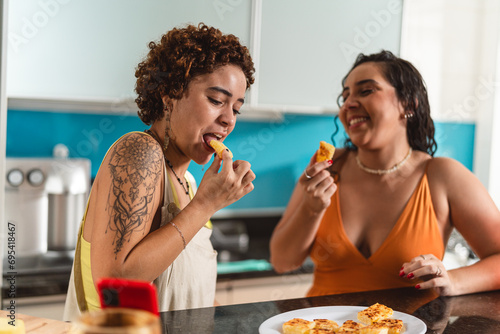 Mulheres jovens na cozinha comendo dadinho de tapioca, um petisco tradicional do Brasil. photo