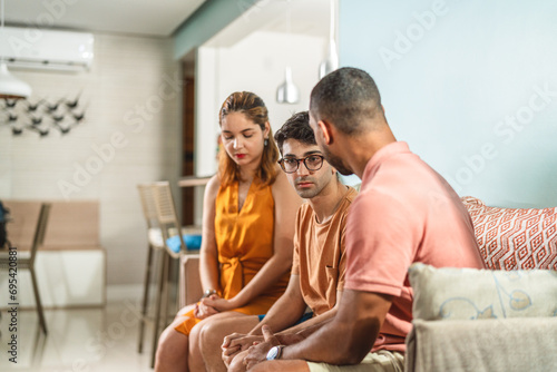 Family sitting on sofa with serious expression having a conversation about a sensitive topic.
