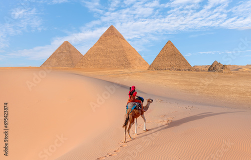 Camels in Giza Pyramid Complex - A woman in a red turban riding a camel across the thin sand dunes - Cairo  Egypt