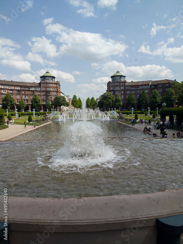 A lively central square with lawns and a large 18th century stone and bronze fountain, in Mannheim, Germany.