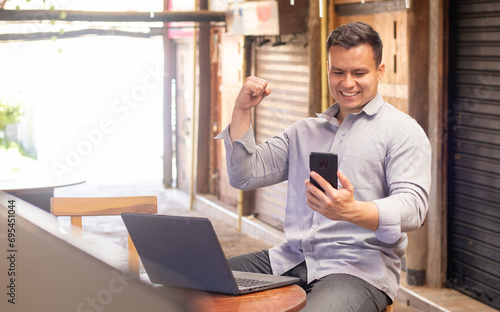 man smiling looking at his cell phone in front of his computer