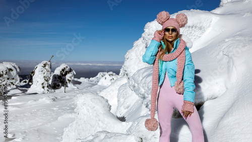 Beautiful happy woman wearing winter outfit and winter fashionable boots and is posing on a sunny day in the mountains.