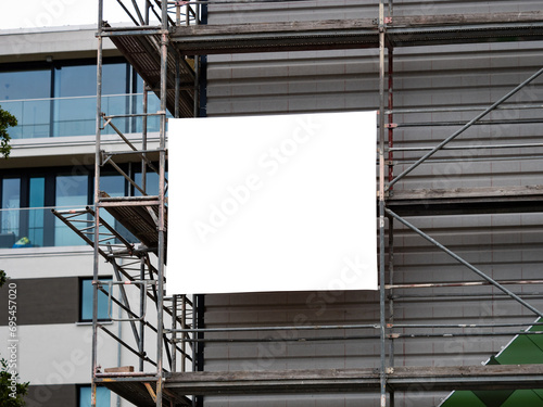 Empty banner on a construction site template. White copy space for a company logo or information of the building. The advertisement is mounted to the scaffolding on the exterior.