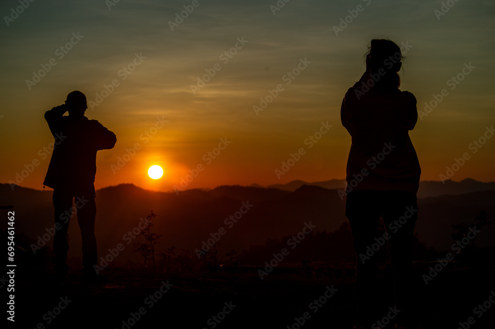 A man and a woman are standing and taking photos of the sunset