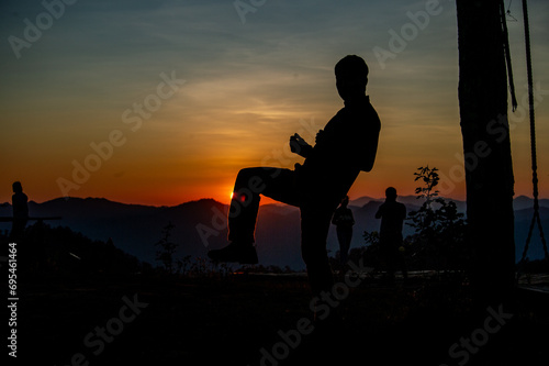 A man making a gesture of playing takraw in front of the setting sun
