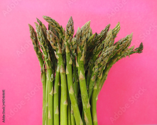 there is a bunch of green raw young asparagus on a pink background. healthy eating. spring vegetables. healthy food. vegan
