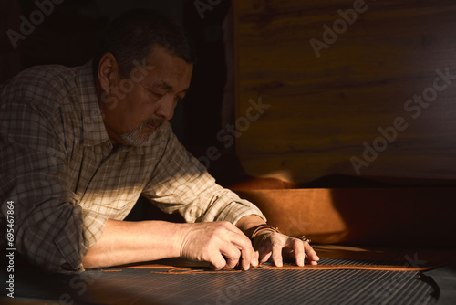 professional artisan makes a new belt, man concentrated on cutting the edges of belt with knife. close up side view photo