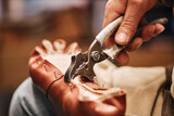 Metallic pliers in hand of male shoemaker fixing upper part of boot to sole while sitting in front of camera and working over client order