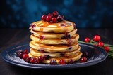  a stack of pancakes covered in syrup and cranberries on a blue plate next to a sprig of fresh cranberries on a dark wooden table.