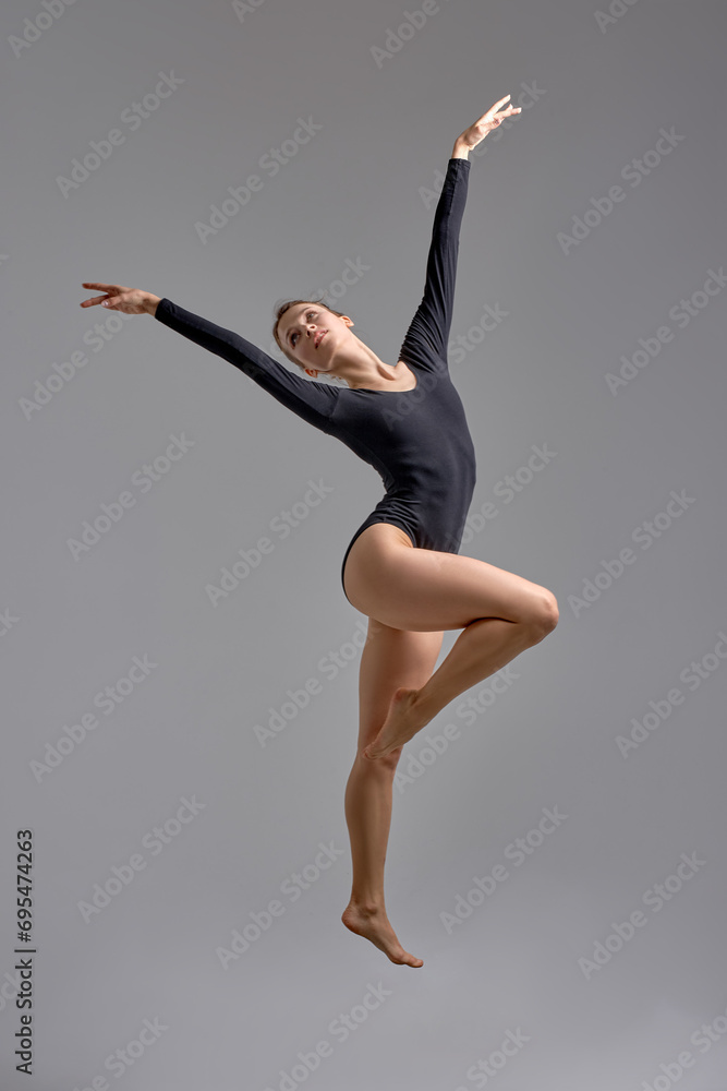 beautiful ginger gymnast with wide raised arms looking up, standing on one leg, full length shot. isolated grey background.