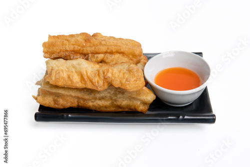 Cakwe or You tiao is a long, golden brown fried dough or Chinese donut. Served on a black plate with a white background photo