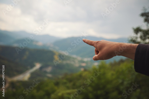 The hand showing direction over mountains. A hiker tourist pointing hand on direction.The hand guide the travel route at mountain. Travel and relax in last holiday. Soft focus and blur.