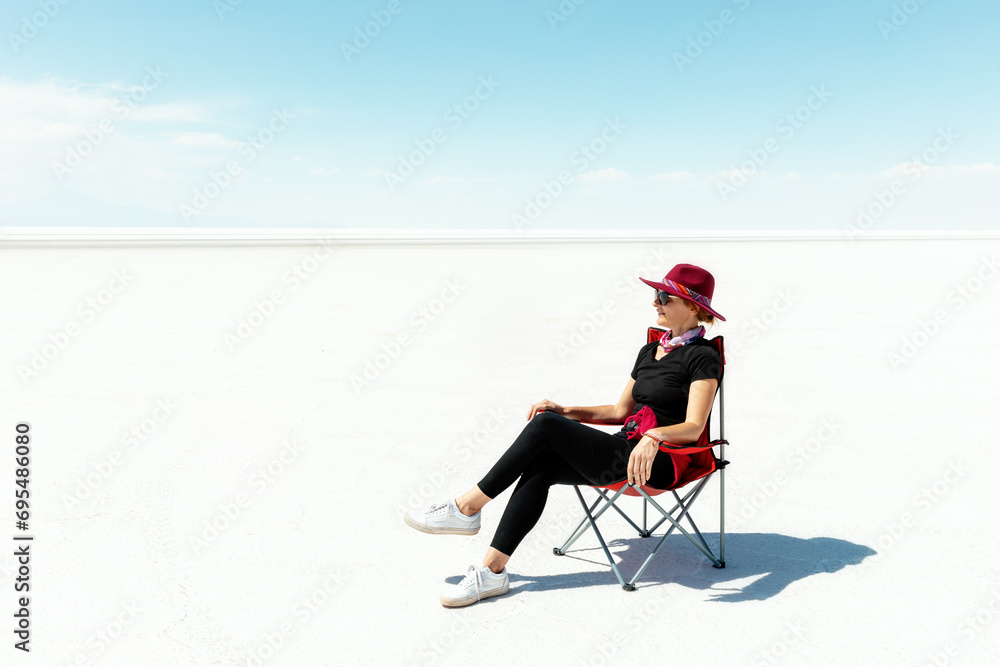 A girl in a cape sits on a folding chair and rests. Salar de Uyuni. Bolivia