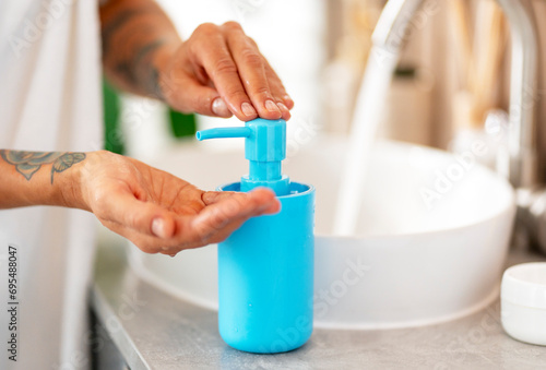 Young woman washing her hands with liquid soap in blue jar, mockup, in bathroom, closeup